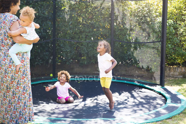 Feliz madre e hijas jugando en el soleado trampolín patio trasero - foto de stock