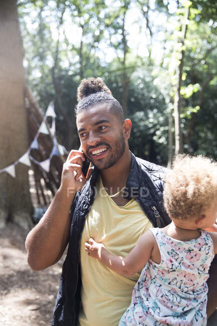 Smiling father holding toddler daughter and talking on smart phone — Stock Photo