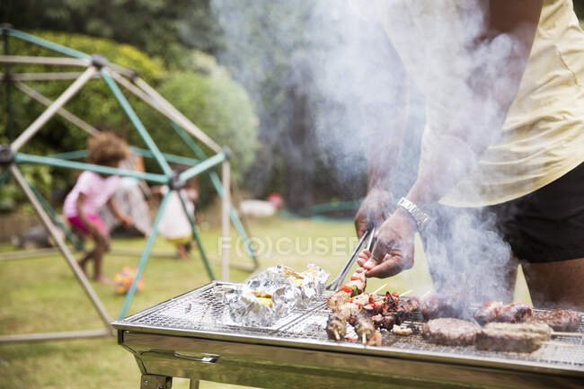 Father barbecuing kebabs at grill in summer backyard — Stock Photo