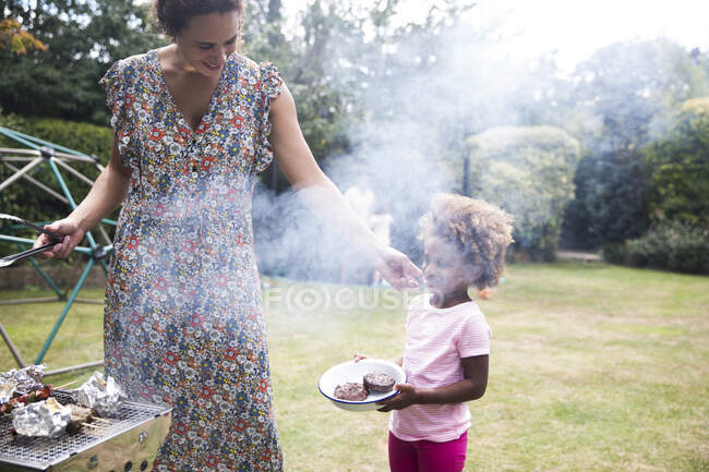 Madre e hija asando en el patio trasero de verano - foto de stock