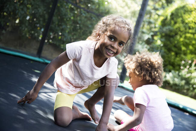 Retrato irmãs despreocupadas jogando no trampolim quintal — Fotografia de Stock
