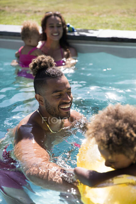 Familia feliz jugando en la soleada piscina de verano - foto de stock