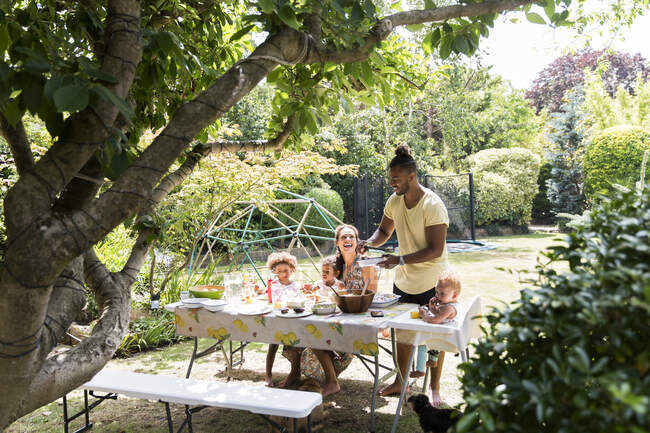 Отец подает барбекю семье за летним столиком на заднем дворе — стоковое фото