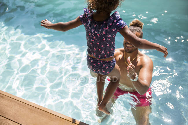 Daughter jumping into arms of father in sunny swimming pool — Stock Photo