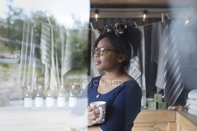 Femme réfléchie propriétaire de magasin boire du café à la fenêtre — Photo de stock