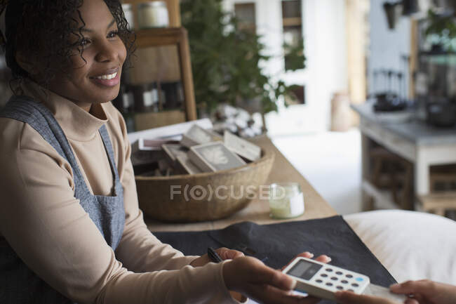 Friendly female shop owner holding credit card reader for customer — Stock Photo