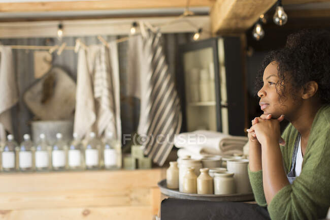 Propietaria de tienda femenina reflexiva mirando hacia otro lado desde detrás del mostrador - foto de stock