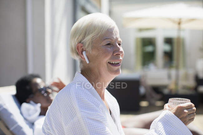 Felice donna anziana con cuffie auricolari sul patio soleggiato dell'hotel — Foto stock