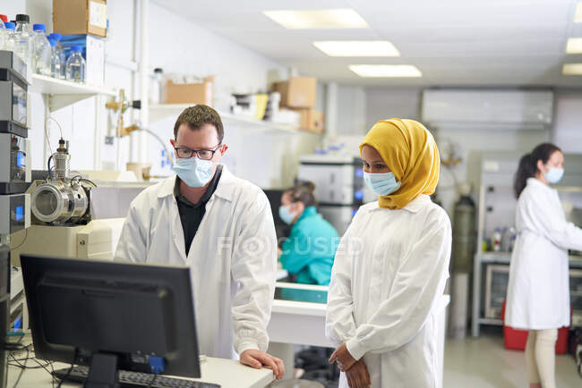 Scientists in face masks working at computer in laboratory — Stock Photo