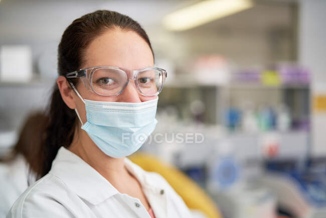 Portrait femme scientifique confiante dans le masque facial en laboratoire — Photo de stock