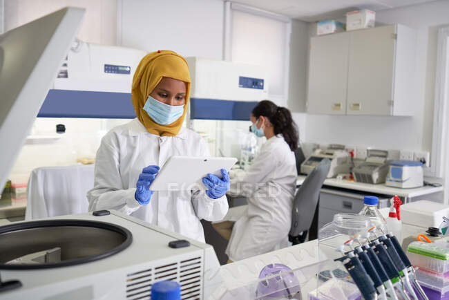 Female scientist in face mask and hijab using digital tablet in laboratory — Stock Photo