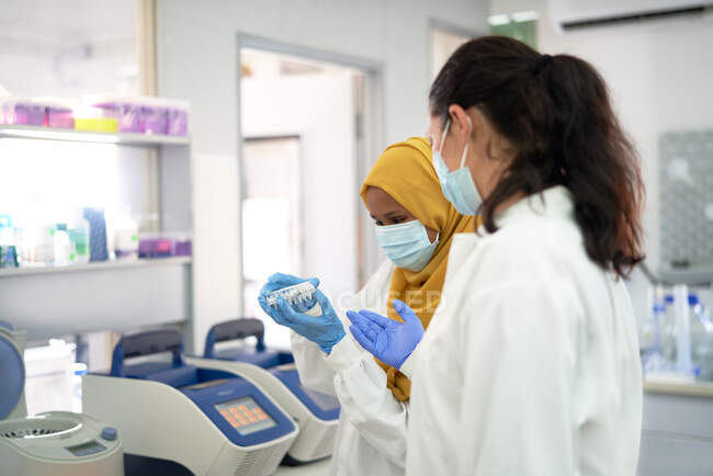 Женщины-ученые в масках для лица с держателем образца в лаборатории — стоковое фото