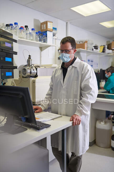 Cientista masculino em máscara facial usando computador em laboratório — Fotografia de Stock