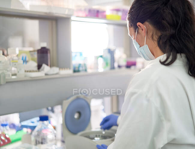 Scienziata in maschera facciale alla centrifuga in laboratorio — Foto stock