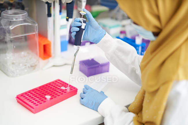 Wissenschaftlerin in Hijab und Gesichtsmaske füllt Pipettenschale im Labor — Stockfoto