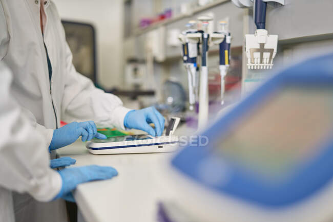 Científicos en guantes de goma utilizando equipos en laboratorio - foto de stock