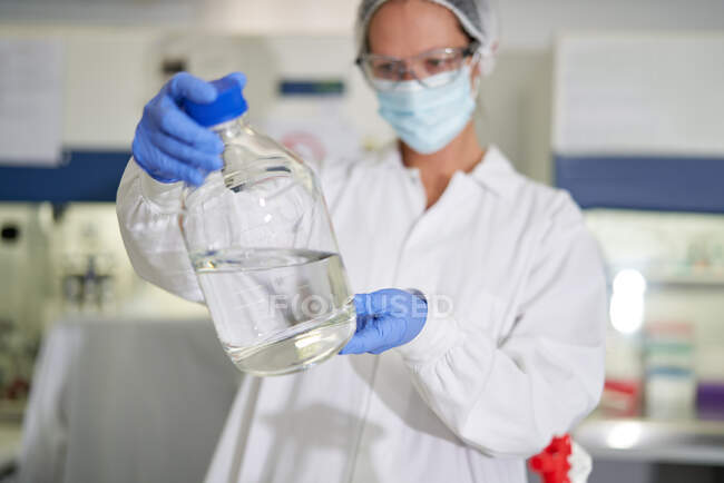 Cientista feminina em máscara facial e luva examinando líquido em laboratório — Fotografia de Stock