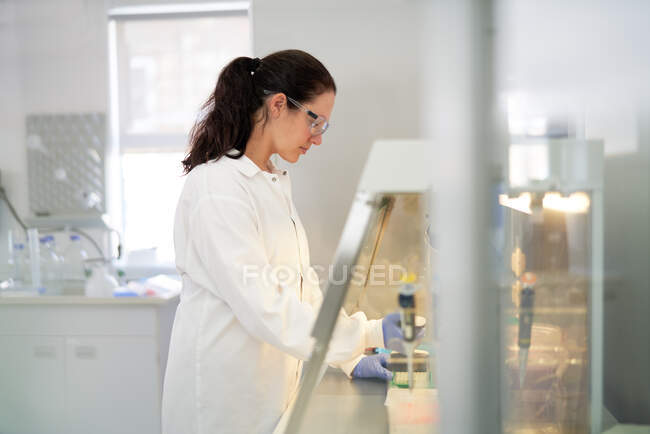 Cientista do sexo feminino que trabalha na capa de fumaça em laboratório — Fotografia de Stock