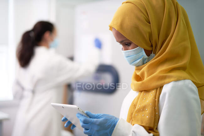 Científica en hijab y mascarilla facial usando tableta digital - foto de stock