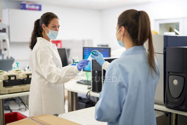 Женщины-ученые в масках для лица держат образец в лаборатории — стоковое фото