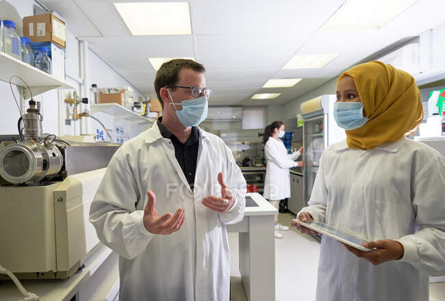 Cientistas em máscaras faciais falando em laboratório — Fotografia de Stock