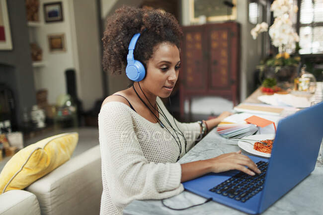Mujer con auriculares trabajando en el portátil en la mesa de comedor - foto de stock