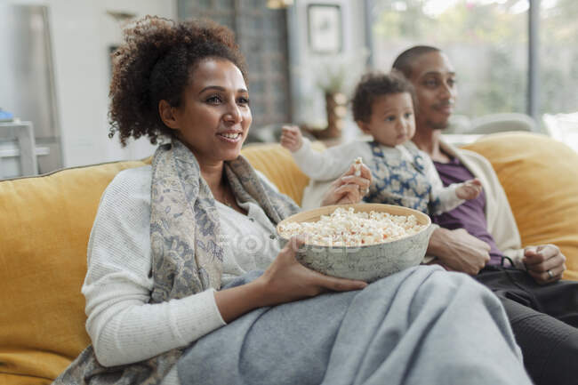 Glückliche Familie schaut Film und isst Popcorn auf Wohnzimmersofa — Stockfoto