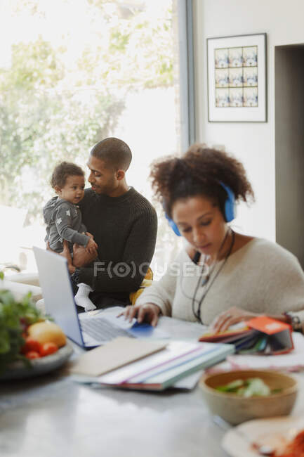 Father holding baby daughter behind working mother at laptop — Stock Photo