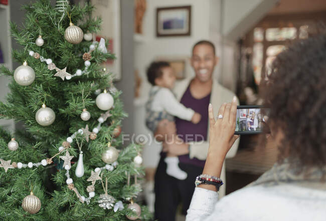 Woman photographing husband and baby daughter by Christmas tree — Stock Photo