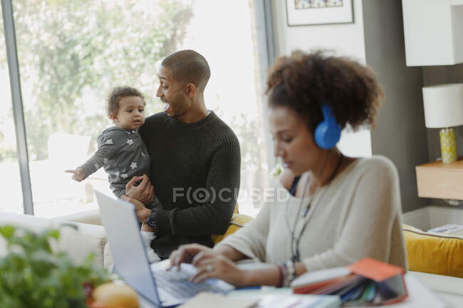 Padre che tiene la figlia dietro la madre che lavora al computer portatile — Foto stock