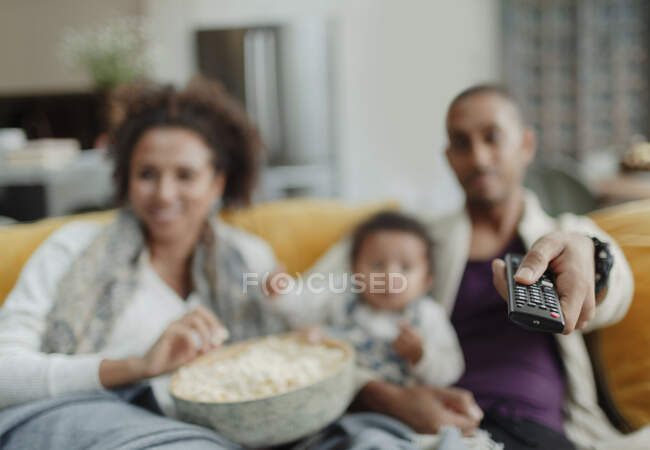 Família com controle remoto assistindo TV com pipoca no sofá — Fotografia de Stock