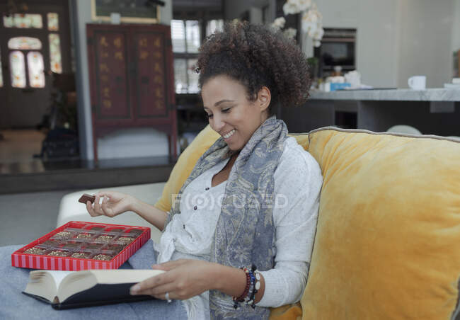 Счастливая женщина читает книгу и ест шоколад на диване — стоковое фото
