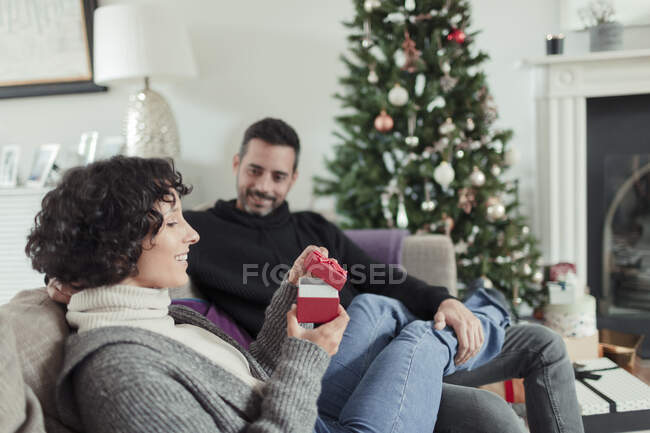 Wife opening Christmas gift from husband on living room sofa — Stock Photo