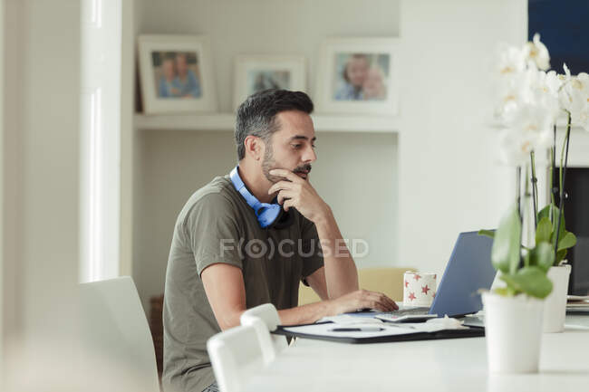 Человек, работающий из дома за ноутбуком на обеденном столе — стоковое фото