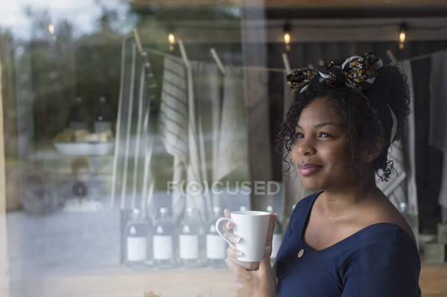 Thoughtful female shop owner drinking coffee at shop window — Stock Photo