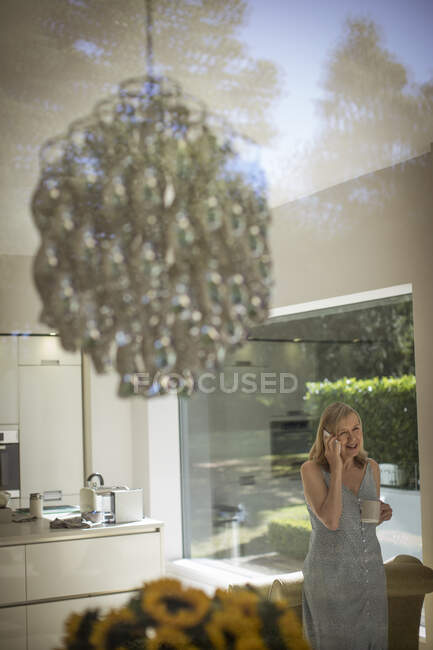 Femme âgée parlant sur téléphone intelligent dans la cuisine avec lustre — Photo de stock
