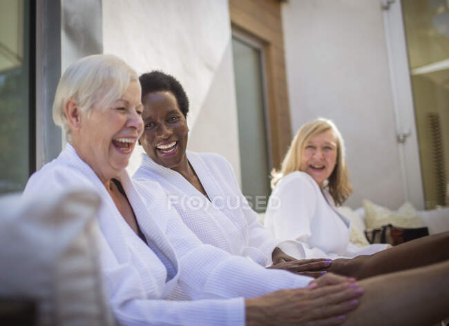 Happy women friends in spa bathrobes laughing on patio — Stock Photo