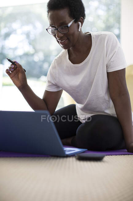 Mature woman with earbud headphones working at laptop on bed — Stock Photo