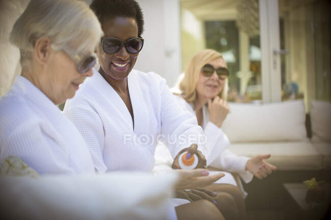 Senior women friends in spa bathrobes and sunglasses on patio — Stock Photo