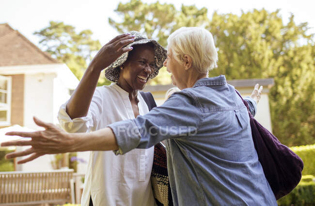 Happy senior women friends greeting and hugging in sunny garden — Stock Photo