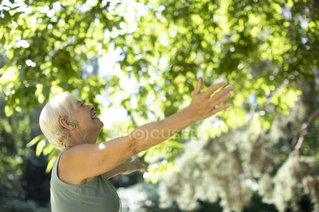 Беззаботная пожилая женщина с распростертыми руками под летними деревьями — стоковое фото