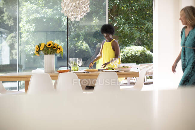 Reife Frau im Kleid deckt Tisch zum Mittagessen im sonnigen Speisesaal — Stockfoto