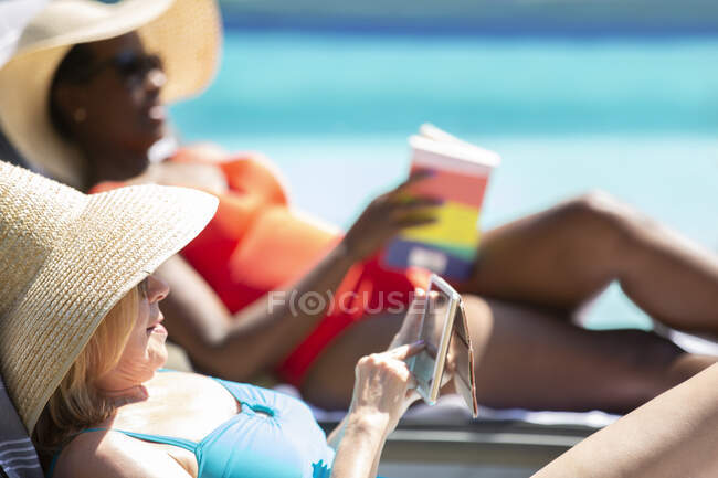Mulher sênior usando telefone inteligente e banhos de sol na piscina de verão — Fotografia de Stock
