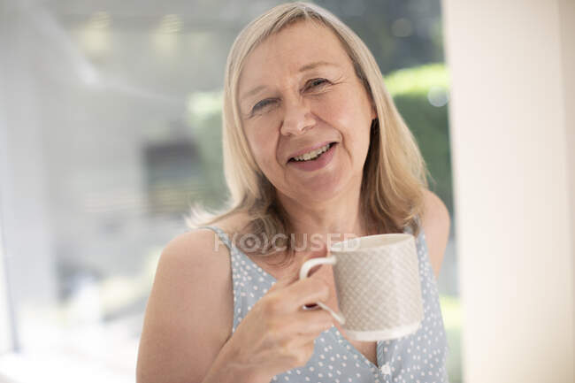 Portrait happy senior woman drinking tea at sunny window — Stock Photo