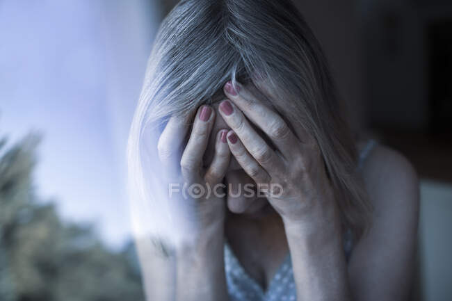 Upset senior woman with head in hands at window — Stock Photo