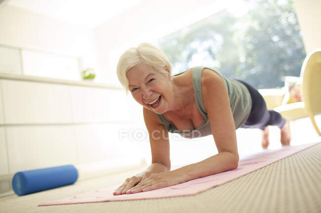 Portrait happy senior woman practicing plank pose on yoga mat at home — Stock Photo
