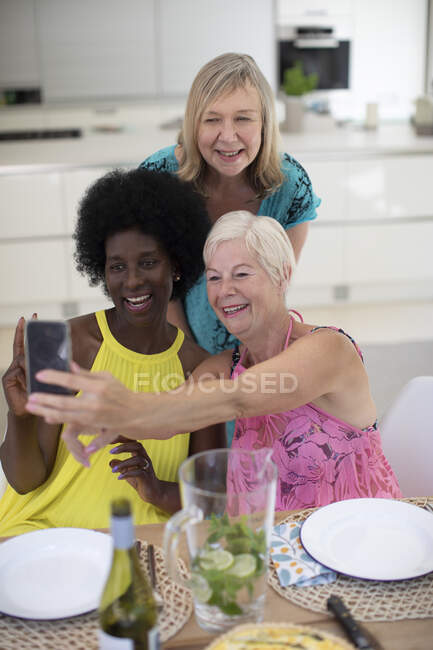 Щасливі старші жінки друзі в сукнях беруть селфі за обіднім столом — стокове фото