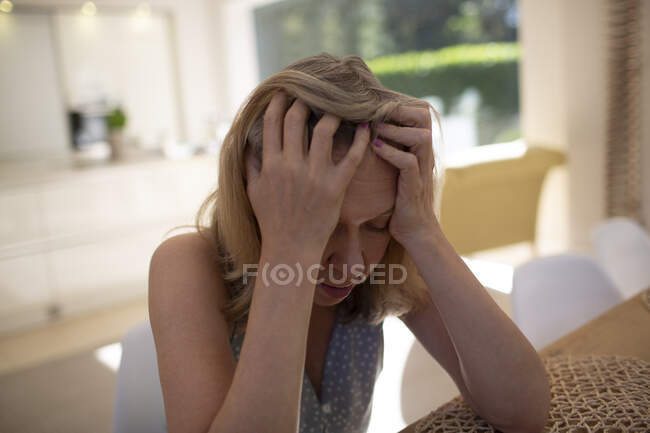Mulher idosa estressada com a cabeça nas mãos na mesa de jantar — Fotografia de Stock