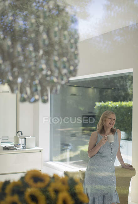 Senior woman drinking tea in sunny dining room with chandelier — Stock Photo