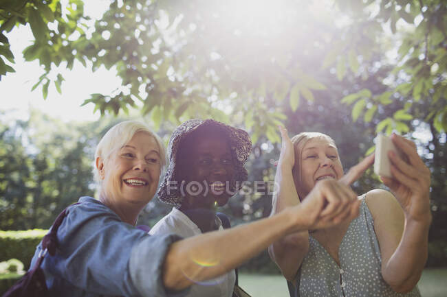 Juguetonas amigas mayores tomando selfie en el soleado jardín de verano - foto de stock